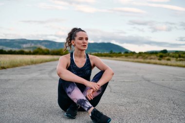 Atletik bir kadın kendini sabah koşusuna hazırlar. Kendini spora adamış ve rutinindeki kararlılığı somutlaştırmıştır. 