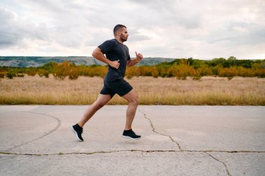 Atletik bir adam güneşin altında koşar, vücudunu yaşam şartlarına şartlandırır. Önündeki yolculuk için azim ve güç yayar.