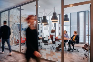 İş ortamının hareketli koşuşturmasında, bir grup genç iş adamı ofislerinin yanındaki koridorda yürürken, meslektaşları içeride iş birliği yaparak,