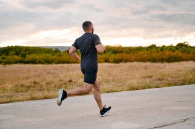Atletik bir adam güneşin altında koşar, vücudunu yaşam şartlarına şartlandırır. Önündeki yolculuk için azim ve güç yayar.