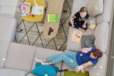 Bir anne ve kızın evdeki koltukta oturup eğlenceli ve büyüleyici bir masa oyunu oynamalarının iç açıcı görüntüsü..