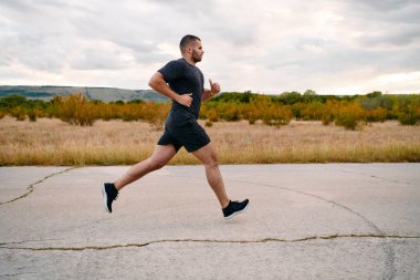 Atletik bir adam güneşin altında koşar, vücudunu yaşam şartlarına şartlandırır. Önündeki yolculuk için azim ve güç yayar.