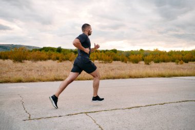 Atletik bir adam güneşin altında koşar, vücudunu yaşam şartlarına şartlandırır. Önündeki yolculuk için azim ve güç yayar.
