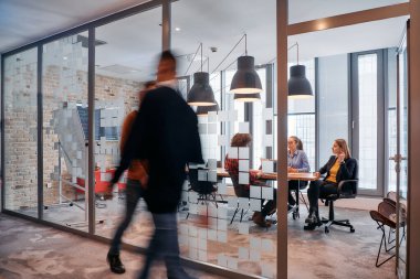 İş ortamının hareketli koşuşturmasında, bir grup genç iş adamı ofislerinin yanındaki koridorda yürürken, meslektaşları içeride iş birliği yaparak,