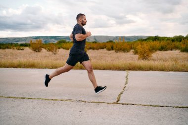 Atletik bir adam güneşin altında koşar, vücudunu yaşam şartlarına şartlandırır. Önündeki yolculuk için azim ve güç yayar.