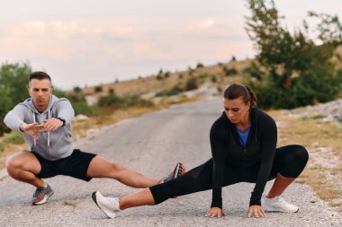 Romantik bir çift, yoğun bir sabah koşusundan sonra vücutlarını esnetirken bir anlık bağ ve rahatlıktan zevk alır..