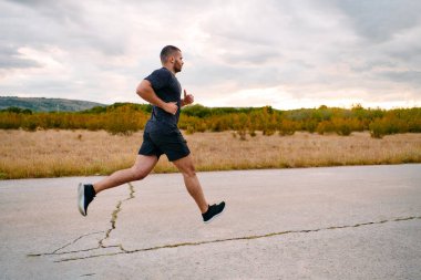 Atletik bir adam güneşin altında koşar, vücudunu yaşam şartlarına şartlandırır. Önündeki yolculuk için azim ve güç yayar.