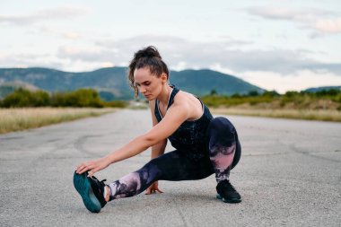 Kararlı bir dişi atlet, engebeli dağ arazilerinde nefes kesici kaya manzaralarıyla çevrili yorucu bir koşudan sonra kaslarını esnetir.. 