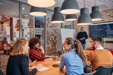 Kurumsal bir ortamda, Afrikalı-Amerikalı bir işadamı bir toplantıya liderlik eder, özenli ekibine tutkuyla bir iş planı sunar, işbirliği ve stratejik düşünmeyi teşvik eder.. 