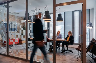 İş ortamının hareketli koşuşturmasında, bir grup genç iş adamı ofislerinin yanındaki koridorda yürürken, meslektaşları içeride iş birliği yaparak,