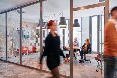 İş ortamının hareketli koşuşturmasında, bir grup genç iş adamı ofislerinin yanındaki koridorda yürürken, meslektaşları içeride iş birliği yaparak,