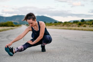 Kararlı bir dişi atlet, engebeli dağ arazilerinde nefes kesici kaya manzaralarıyla çevrili yorucu bir koşudan sonra kaslarını esnetir.. 