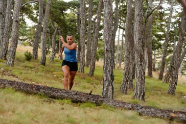 Korkusuz bir kadın korkusuzca tehlikeli orman arazisinde geziniyor, azim ve zarafetle ahşap engellerin üzerinden atlıyor, maceracı ruhunu ve atletik hünerini sergiliyor.