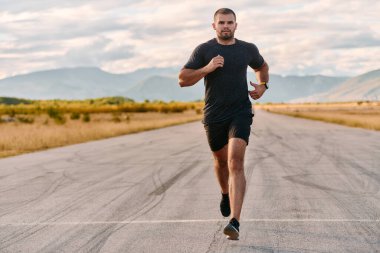 Atletik bir adam güneşin altında koşar, vücudunu yaşam şartlarına şartlandırır. Önündeki yolculuk için azim ve güç yayar.