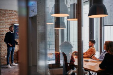 Kurumsal bir ortamda, Afrikalı-Amerikalı bir işadamı bir toplantıya liderlik eder, özenli ekibine tutkuyla bir iş planı sunar, işbirliği ve stratejik düşünmeyi teşvik eder.. 