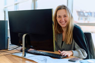 Sarışın bir iş kadını modern bir ofiste bilgisayarın başında oturmuş, ahşap işleme makinesi için bir yazılım programı geliştiriyor..