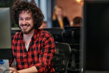 Afro saç stili ve ekose gömlekli bir programcı, modern ofis ortamındaki bir bilgisayarda özenle kodluyor.