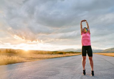 Yalnız bir sporcu, çarpıcı bir günbatımının arka planına zarifçe uzanırken yakalanır. Silueti yoğun bir koşudan sonra kendini adamışlık ve dayanıklılığın bir göstergesidir. 