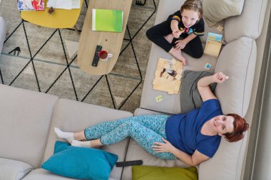 Bir anne ve kızın evdeki koltukta oturup eğlenceli ve büyüleyici bir masa oyunu oynamalarının iç açıcı görüntüsü..