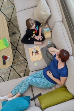 Bir anne ve kızın evdeki koltukta oturup eğlenceli ve büyüleyici bir masa oyunu oynamalarının iç açıcı görüntüsü..