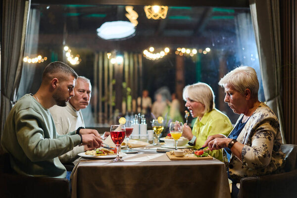 A group of family friends, comprising a young grandson and older individuals, share a delightful dinner in a modern restaurant, exemplifying the concept of healthy aging through intergenerational