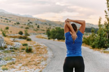 Kararlı bir dişi atlet, engebeli dağ arazilerinde nefes kesici kaya manzaralarıyla çevrili yorucu bir koşudan sonra kaslarını esnetir.. 