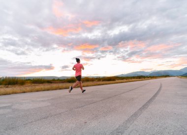 Kararlı bir sporcu güneşin altında kendinden emin bir şekilde koşar. Çevresi göz kamaştırıcı doğal manzaralarla çevrilidir. Zindelik arayışında güç ve direnç gösterir. 