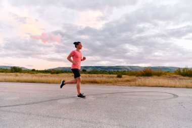 Kararlı bir sporcu güneşin altında kendinden emin bir şekilde koşar. Çevresi göz kamaştırıcı doğal manzaralarla çevrilidir. Zindelik arayışında güç ve direnç gösterir. 