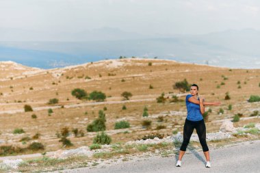 Kararlı bir dişi atlet, engebeli dağ arazilerinde nefes kesici kaya manzaralarıyla çevrili yorucu bir koşudan sonra kaslarını esnetir.. 