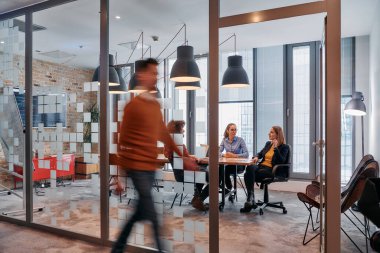 İş ortamının hareketli koşuşturmasında, bir grup genç iş adamı ofislerinin yanındaki koridorda yürürken, meslektaşları içeride iş birliği yaparak,