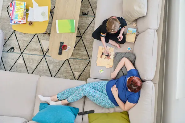 Bir anne ve kızın evdeki koltukta oturup eğlenceli ve büyüleyici bir masa oyunu oynamalarının iç açıcı görüntüsü..