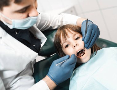 İnsanlar, tıp, stomatoloji, teknoloji ve sağlık hizmetleri kavramı. Klinikte küçük bir kızla çalışan profesyonel erkek dişçi..