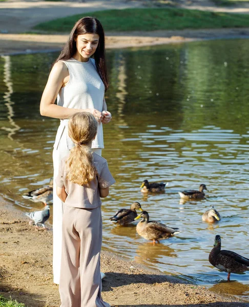 Mom and daughter feeding ducks in a park on the lake. Summer time.