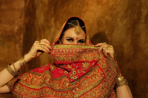 Beautiful indian female. Young hindu woman model with traditional jewelry. Indian costume red saree. Indian or Muslim woman covers her face.