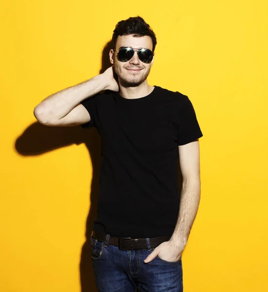 Young handsome fashionable male model wearing sunglasses standing against yellow background