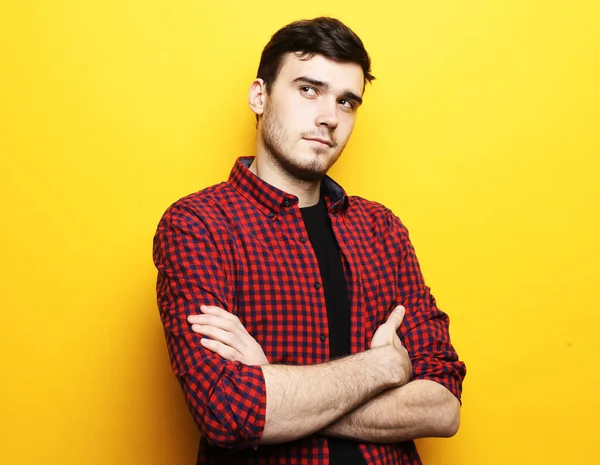 Young handsome fashionable male model with crossed arms against yellow background