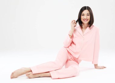 Pembe pijama giymiş güzel Asyalı kadın beyaz arka planda oturuyor, yaşam tarzı kavramı.