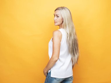 Uzun gümüş saçlı, güzel, yaşlı bir kadın yarım yamalak duruyor. Bayan muhteşem saçlarını gösteriyor. Sarı arkaplan portresi.