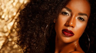 Parlak makyajlı güzel bir Afrikalı kadın altın bir arka plana poz veriyor. Portreyi kapat.