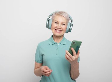 Mutlu, kısa saçlı, kablosuz kulaklıklı, gri arka plan üzerinden cep telefonu kullanan mutlu bir kadın.