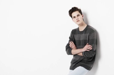 Sıradan kazak ve kot pantolon giyen genç bir erkek model beyaz arka planda poz veriyor.