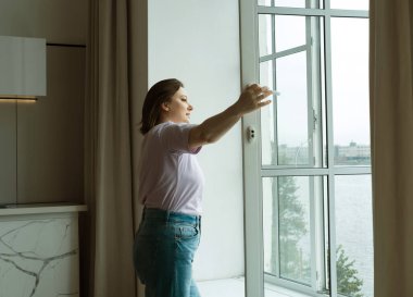 Tombul kadın sabahın erken saatlerinde pencereyi açar, temiz havanın ve yaşam tarzının tadını çıkarır..