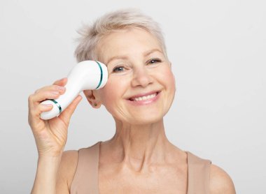 Güzel yüz portresi. Kısa saçlı hoş ve güzel bir kadın. Yüzüne masaj aleti takıyor.