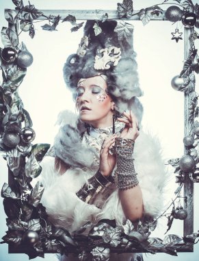 Parti, Noel ve halk konsepti: Gümüş sanatsal makyajlı, peruklu, Noel süslemeleri ile süslenmiş gümüş çerçevede poz veren yaratıcı görünümlü genç kadın. Kış Portresi. Kar Kraliçesi.