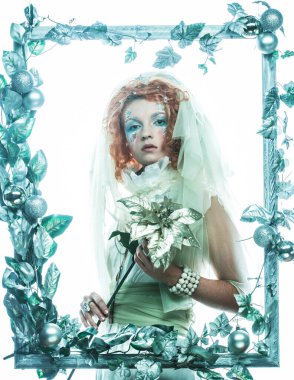 Parti, noel ve halk konsepti: Noel karnavalı için kostüm giymiş güzel kızıl bir kadın Noel süslemeleri çerçevesinde poz veriyor ve elinde bir çiçek tutuyor. Kış stili, Kar Kraliçesi.