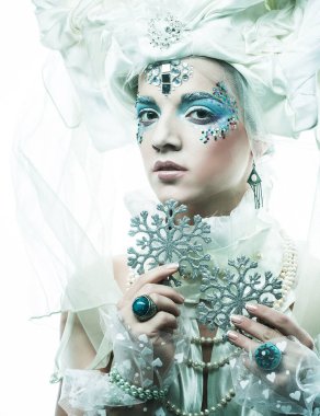 Parti, noel ve halk konsepti: Yeni yıl tarzında yaratıcı makyajlı genç güzel bir kadın yüzünde gümüş kar taneleri tutuyor. Kar Kraliçesi, peri.