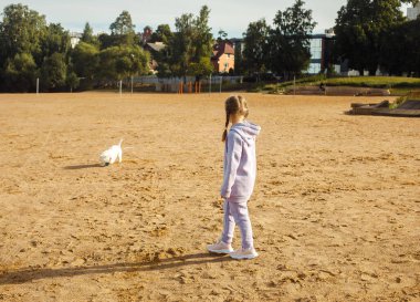 Yedi yaşında at kuyruklu bir kız gölün yanındaki sahilde batı dağlık beyaz bir teriyerle oynuyor. Hayvan dostluğu ve mutlu çocukluk kavramı..