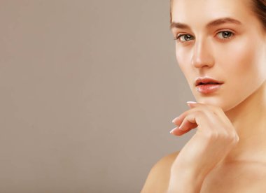 Temiz tenli güzel genç bir kadın gri arka planda yüzüne dokunuyor. Kozmetik, güzellik ve kaplıca konsepti.