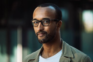 Şehirde ciddi bir ifadeyle gözlük takan ciddi bir Afrikalı gencin ön portresini kapat.