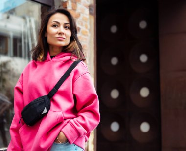 Pembe kazak ve kot pantolon içinde kameraya bakıp eğlenirken poz veren güzel, şık Asyalı genç bir kadın. Gençlik ve moda kavramı.